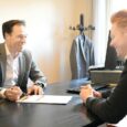 Kaksi miestä keskustelee asiakirjasta toimistopöydän ääressä