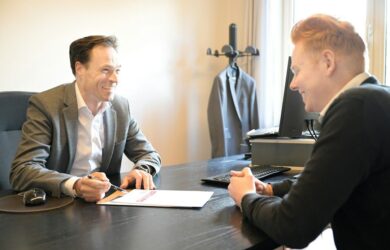 Kaksi miestä keskustelee asiakirjasta toimistopöydän ääressä